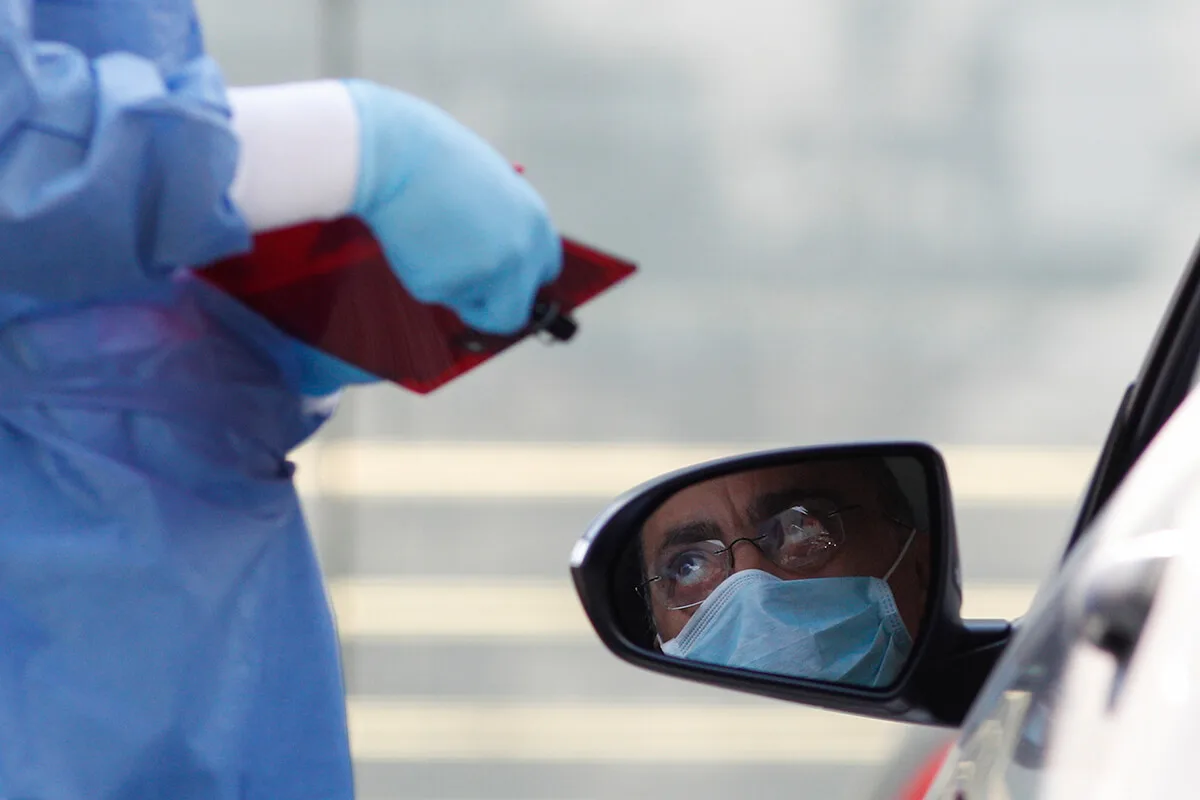 doctor taking down information from man wearing a mask in a car