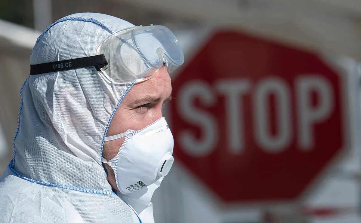 person in protective medical gear in front of a stop sign