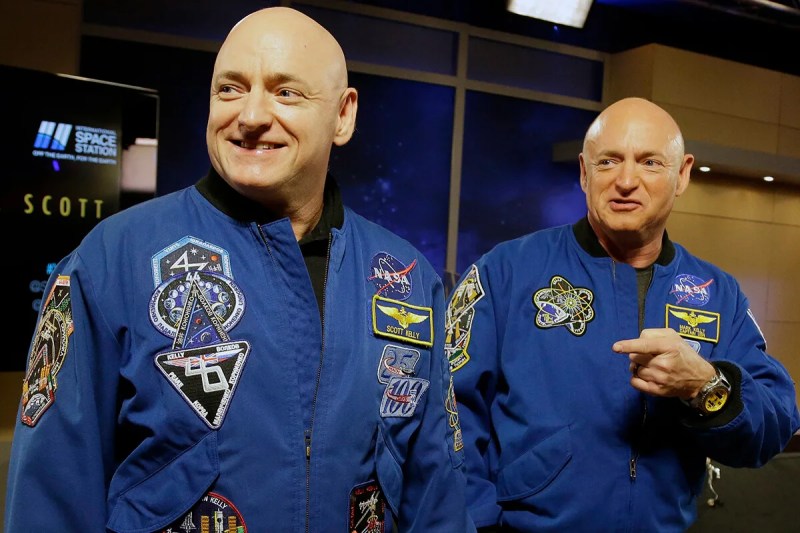 Scott and Mark Kelly standing next to each other wearing spacesuits