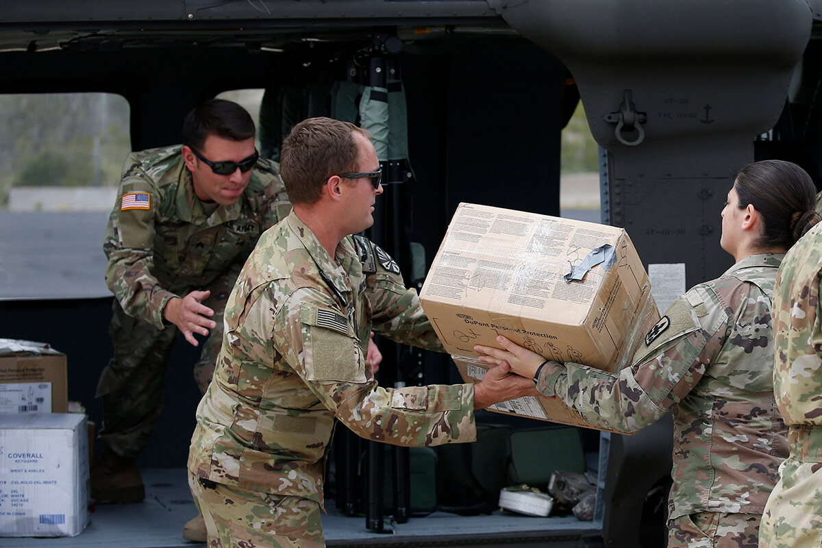 Three National Guard members unloading boxes from helicopter