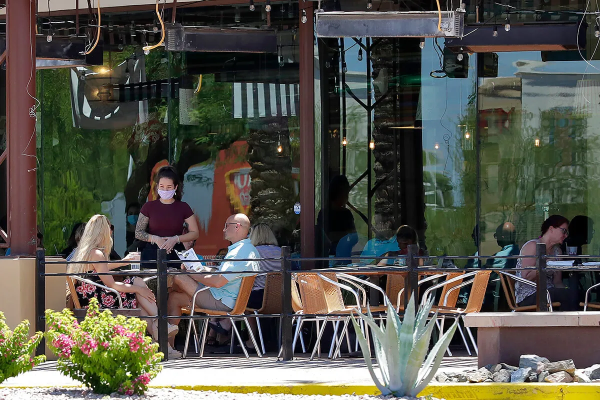 two people sitting at table at restaurant while waitress in mask speaks with them