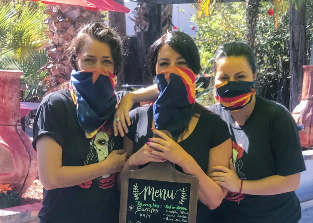 three women wearing face masks holding a menu