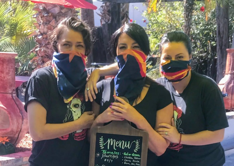 three women wearing face masks holding a menu