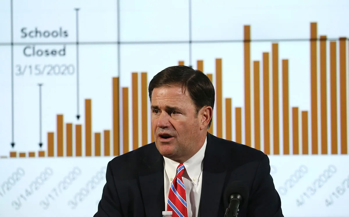 Gov. Ducey sitting in front of a graph of coronavirus-related numbers