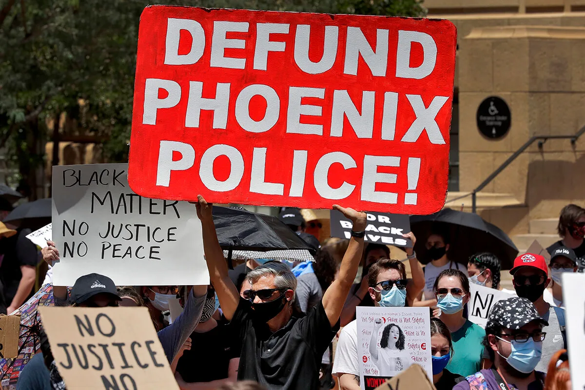 protester holding sign that says "Defund Phoenix Police"