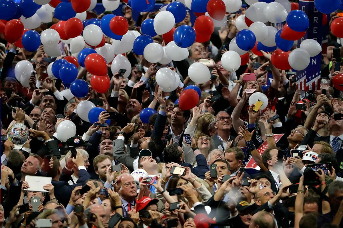 large crowd of people cheering as red, white and blue balloons fall
