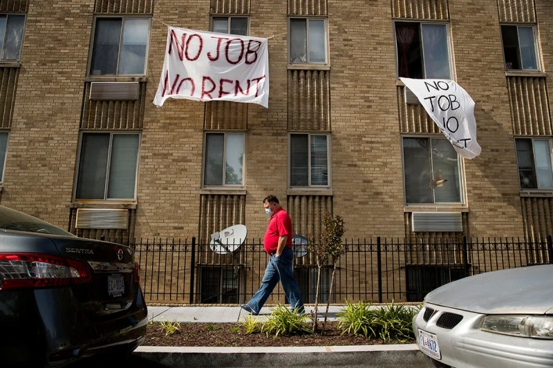 man walking past apartment buildings, which has signs posted on it saying "no job no rent"
