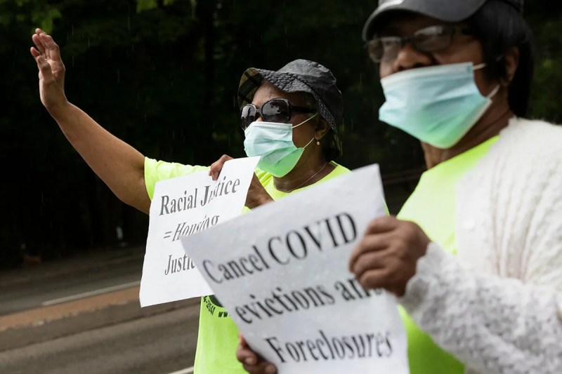 two masked women holding signs asking that COVID-19 evictions be canceled