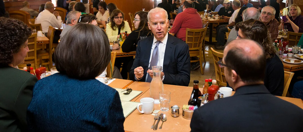 Joe Biden talking to a man and a woman at a restaurant table