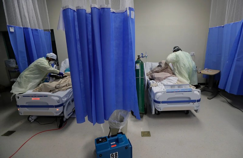 medical workers attending to two COVID patients in hospital beds