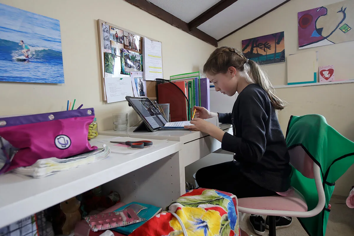 child working on her laptop at desk in her bedroom