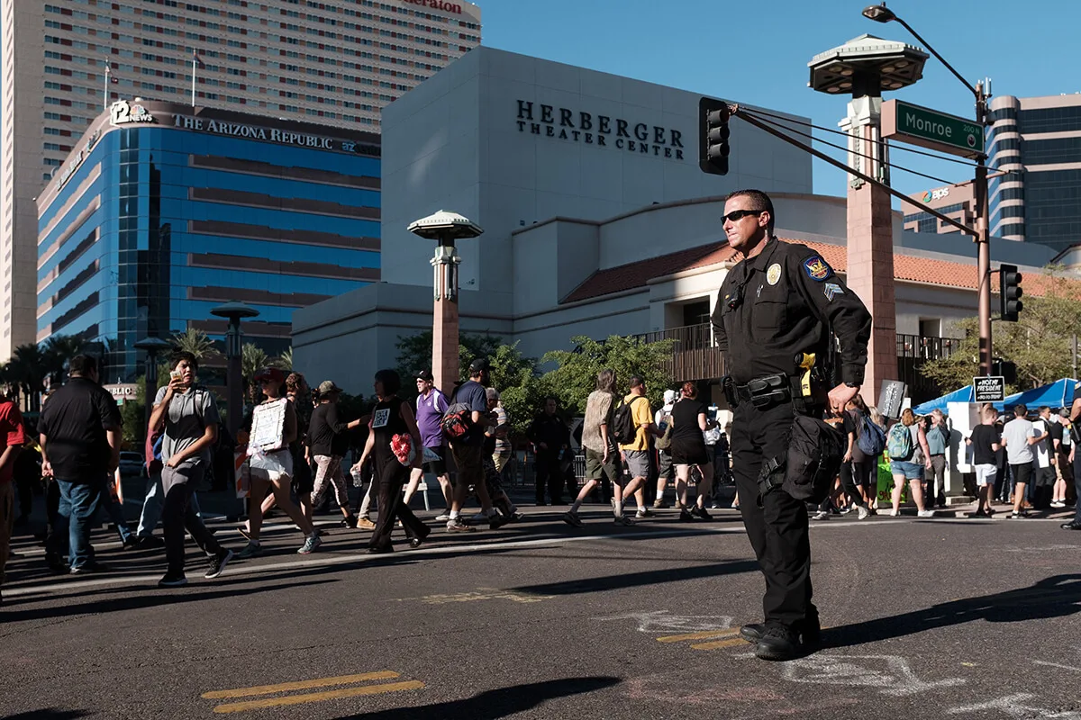 a police officer stands in downtown Phoenix as a group of protesters walks past