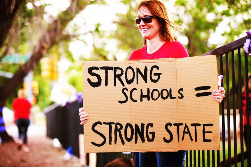 woman holding sign that says "strong schools equals strong state"