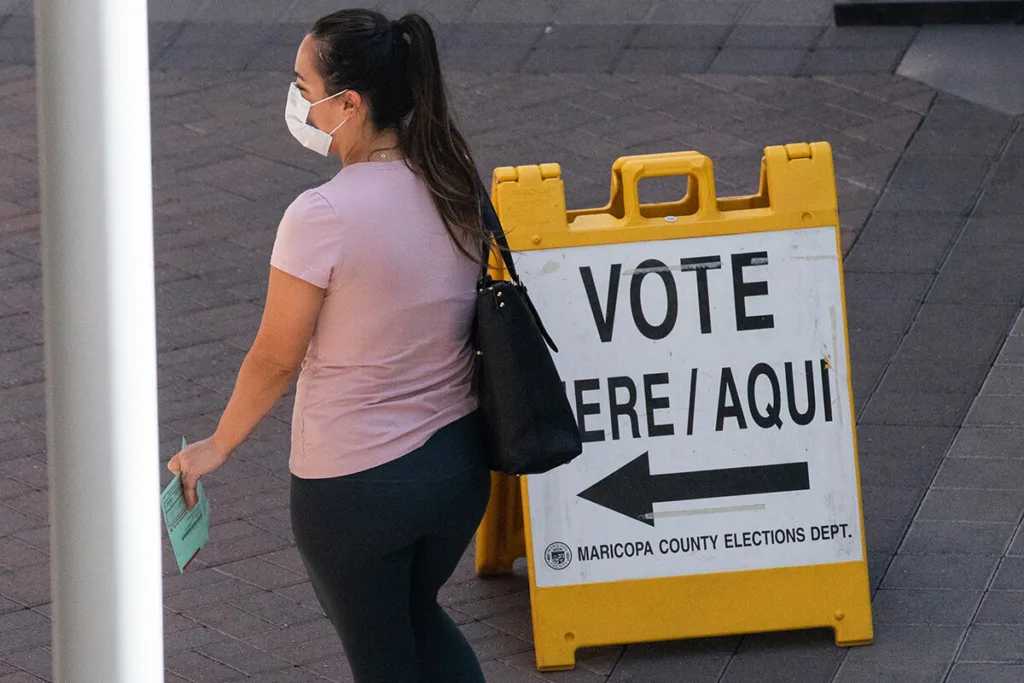 woman wearing masks walks past vote here sign