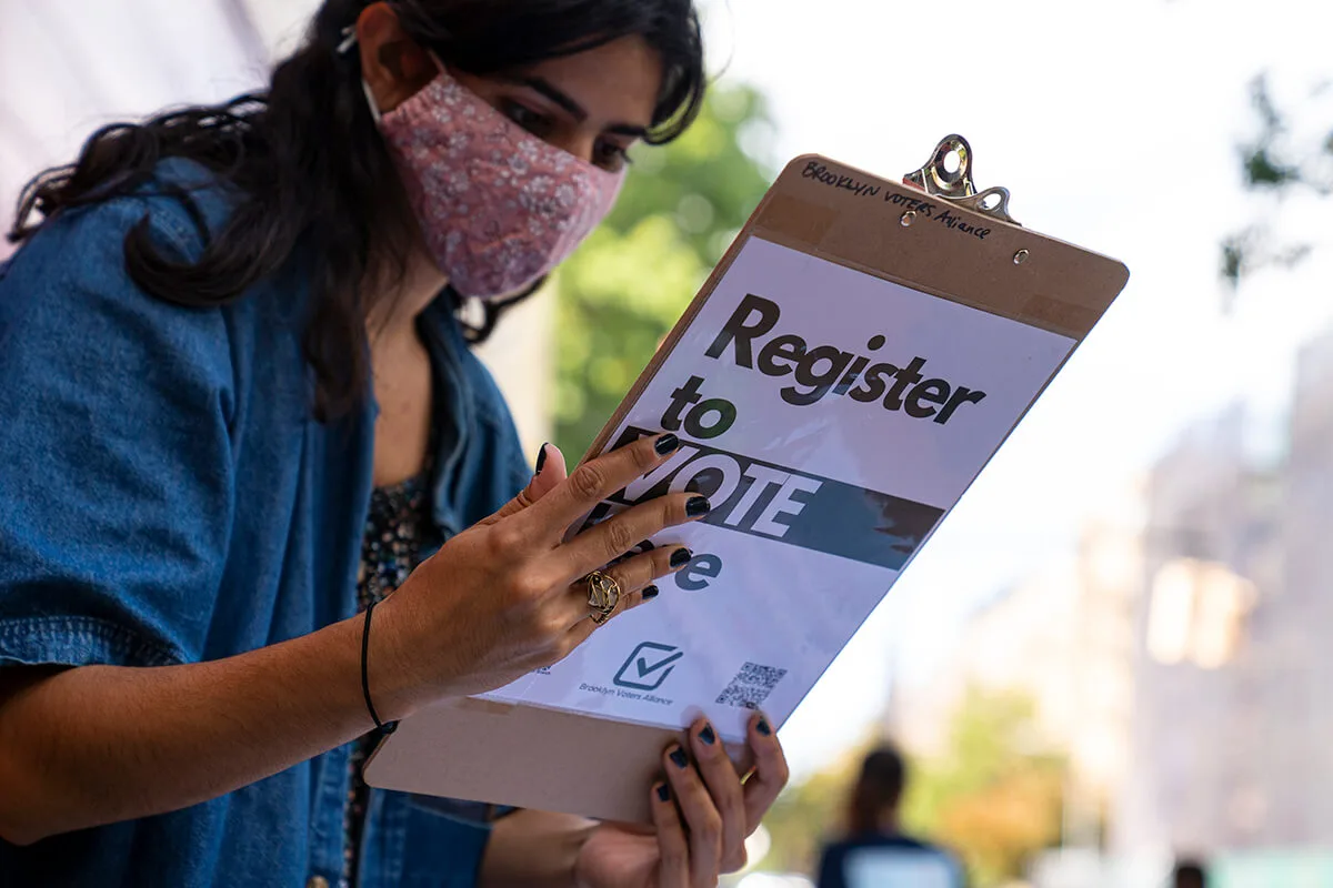 woman holds clipboard that says "register to vote here"