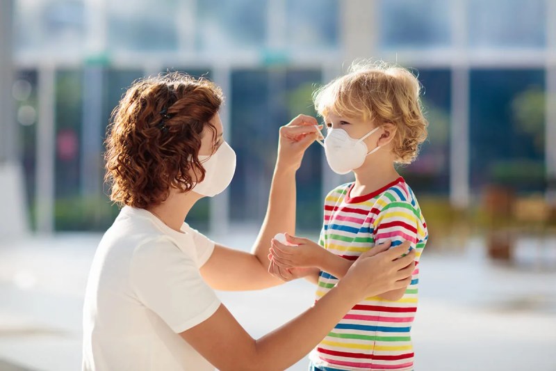 woman wearing masks kneeling and adjusting mask on young boy's face