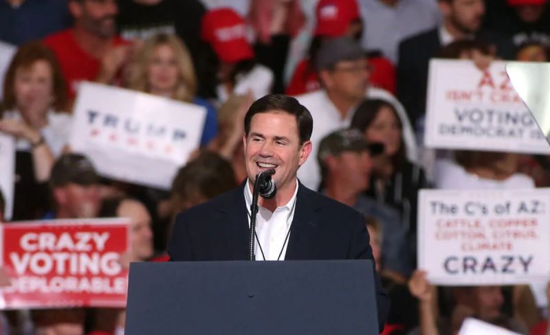Gov. Doug Ducey smiling as he stands at podium with crowd behind him
