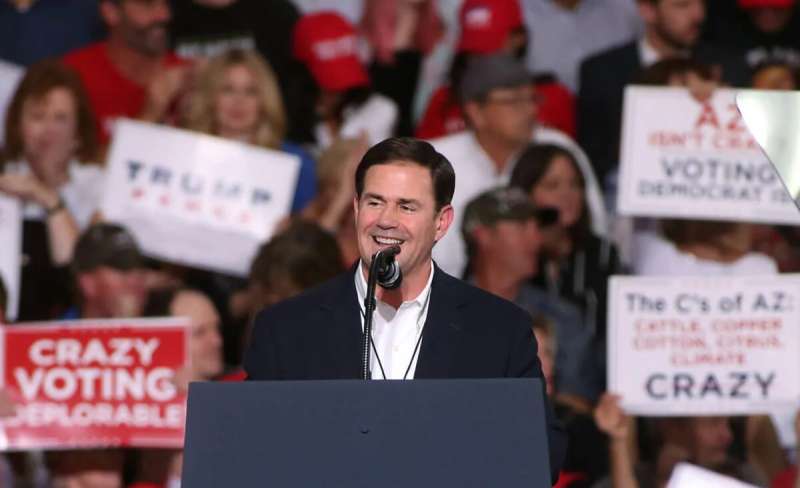 Gov. Doug Ducey smiling as he stands at podium with crowd behind him