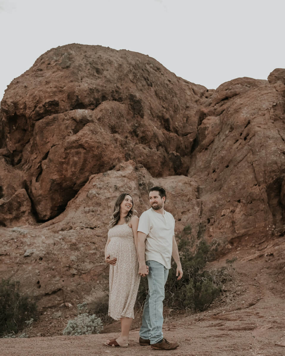 pregnant woman and male partner standing in front of Papago Park rock formation 