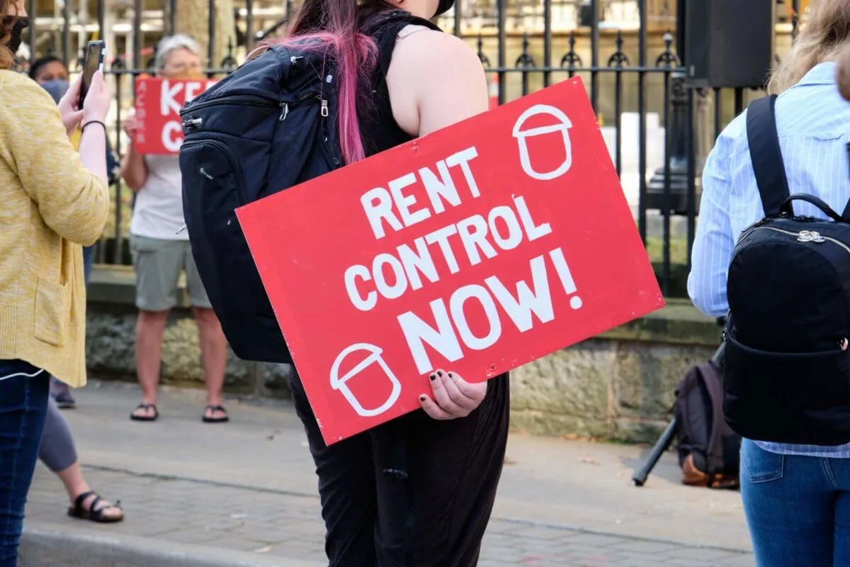 woman holding a sign that says "rent control now"
