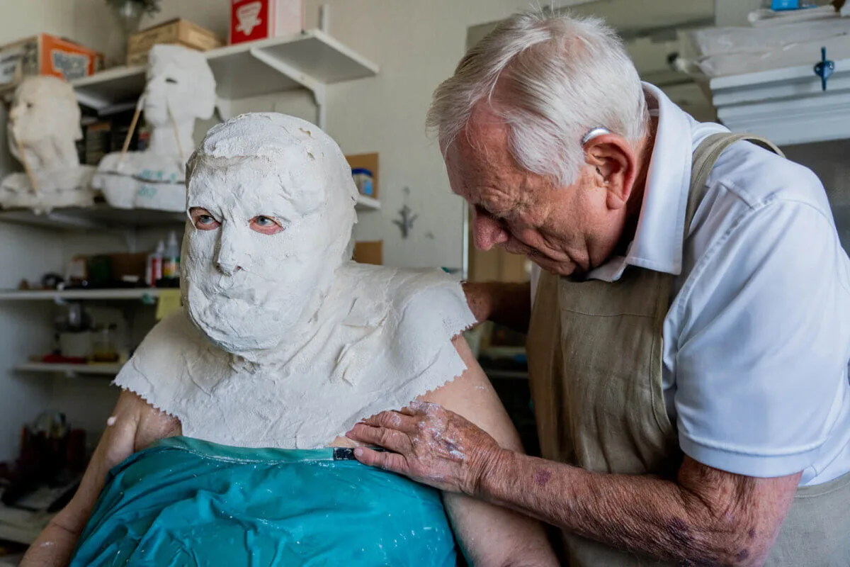 man with plaster mask covering his face as man begins to peel it away
