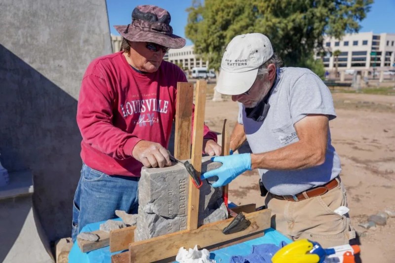 two men working on piecing an old grave marker back together