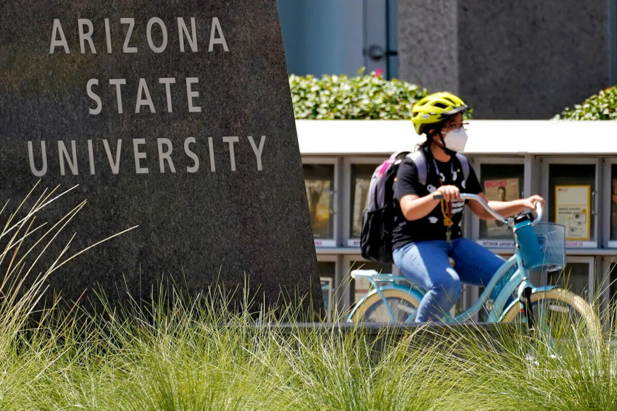 masked student bikes past ASU sign