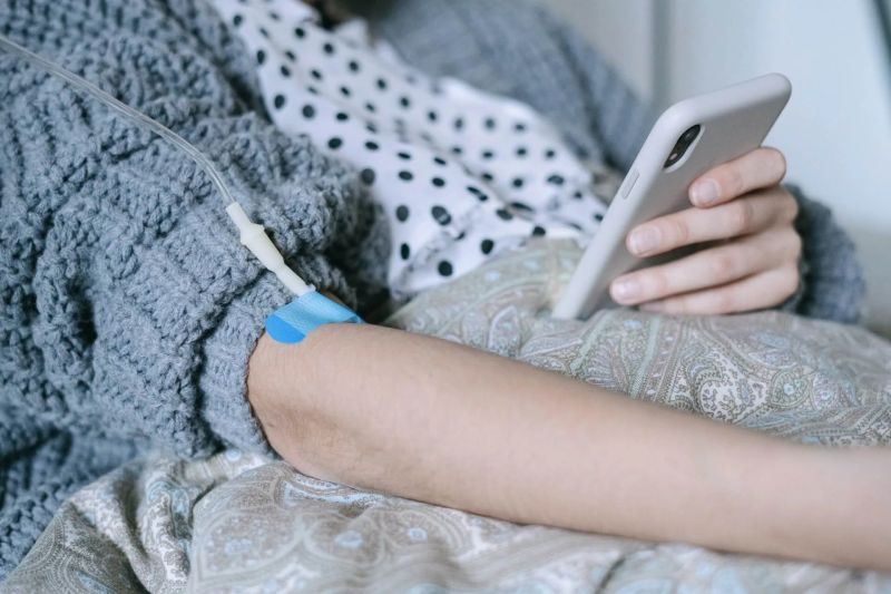 woman looking at phone while having chemo IV in arm