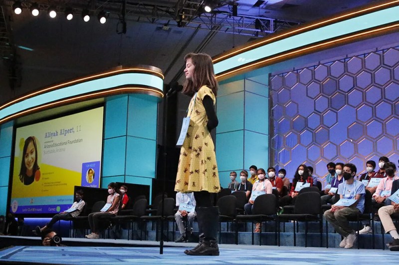 young girl stands on stage wearing a yellow bee-patterned dress