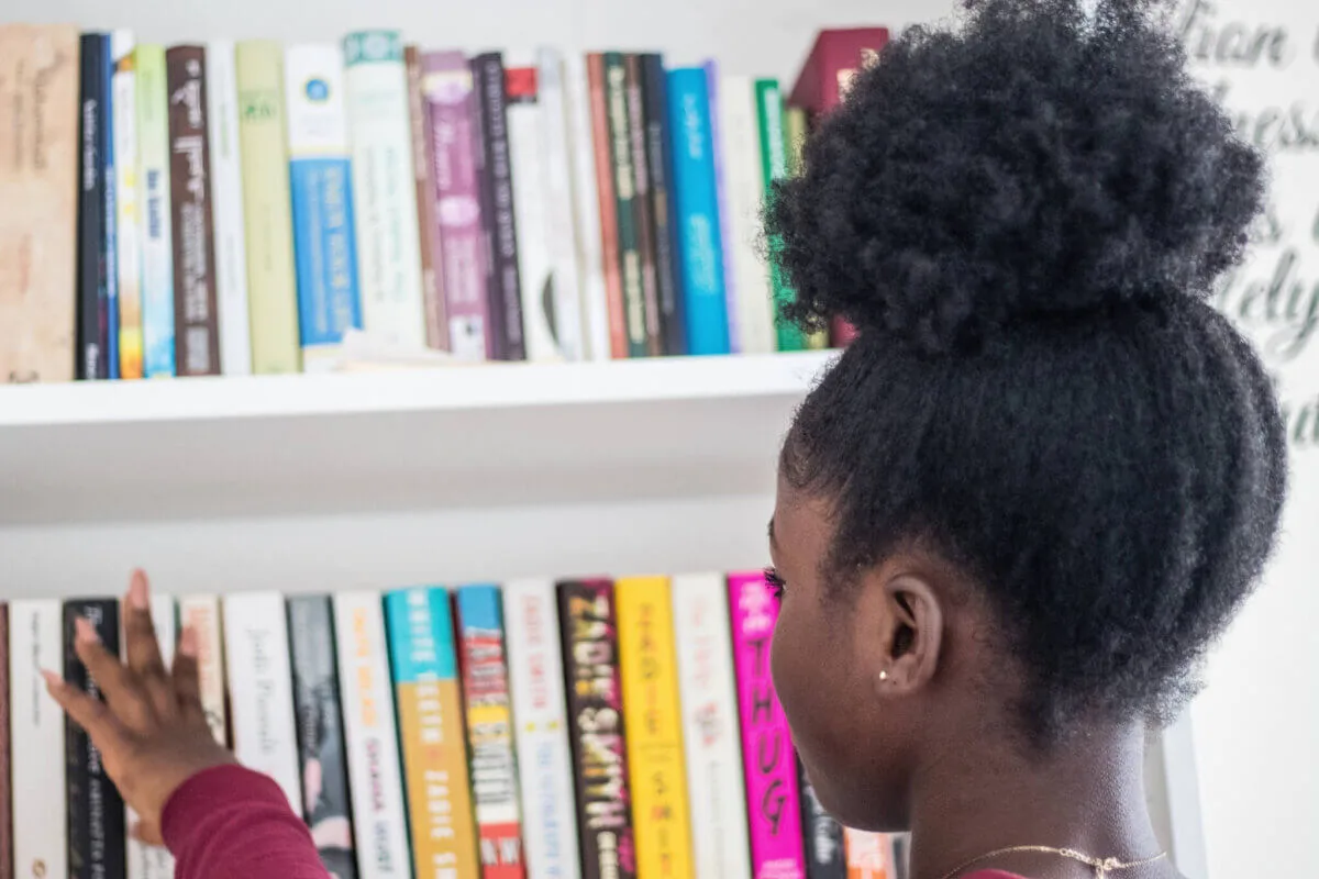 young black girl looks at bookshelf with hand outstretched to choose a book