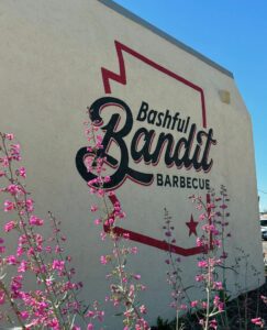 The outside of the building at Bashful Bandit BBQ with a logo and pink flowers.