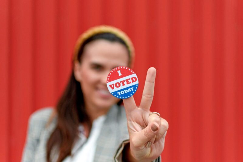 Selective focus image of young woman against red background. Woman is holding voting sticker reading "I voted today."
