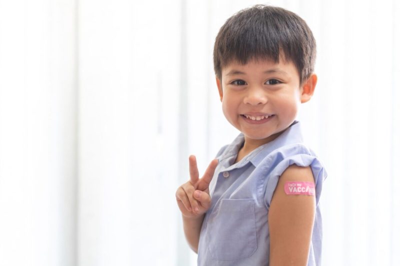 Portrait of happy smile vaccinated little asian kid boy children ages 5 to 11 years old posing show arm with medical plaster after Injection vaccine Covid-19 protection.coronavirus vaccination kid