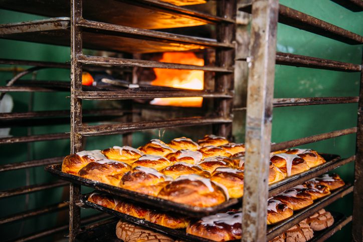 Trays full of sweet bread cooling off beside an oven of a small Mexican bakery.