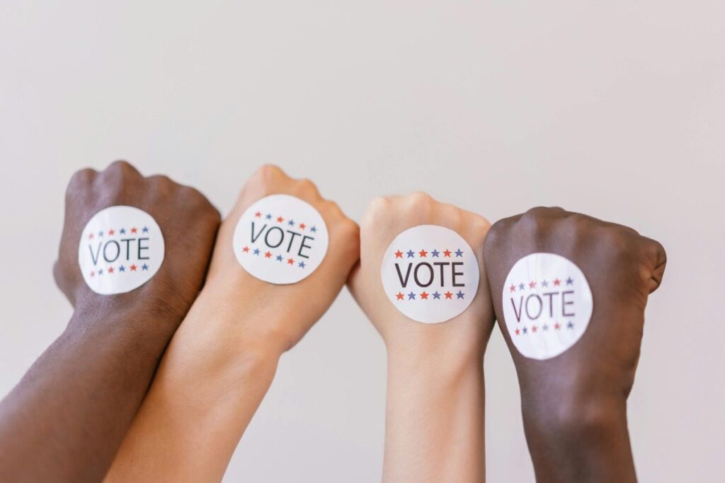 A group of four raised fists, each with a "Vote" sticker on the back.