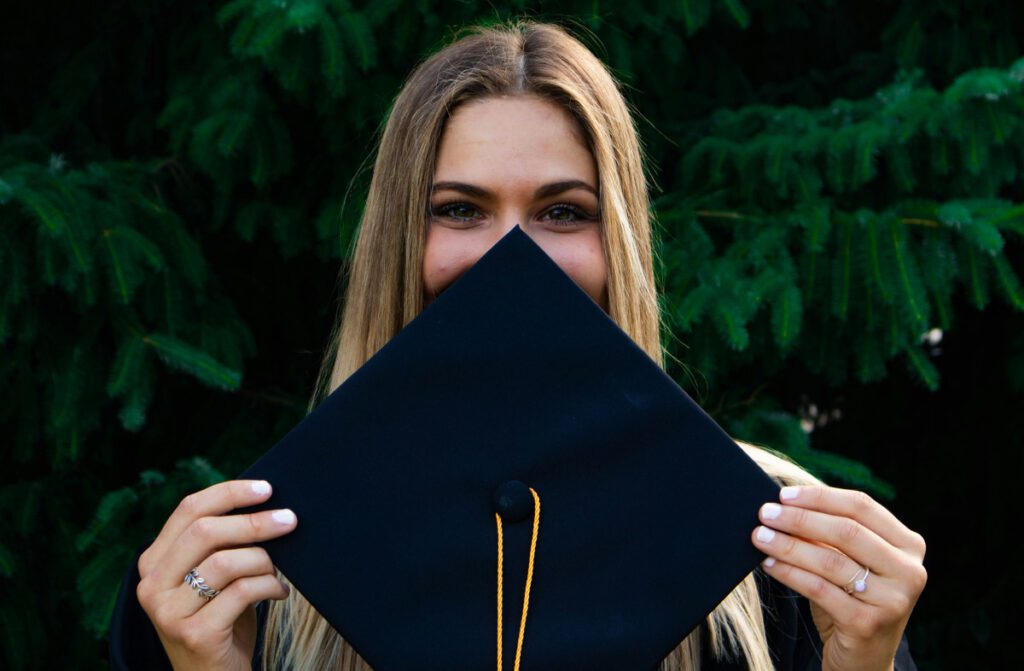 Young blonde girl smiling behind a college graduation cap.