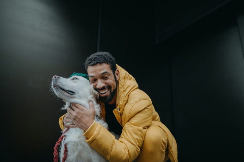 A man in a yellow jacket hugs his dog.