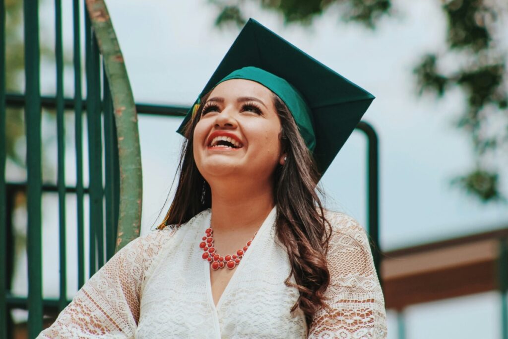 Hispanic student looking upward and smiling while wearing a green graduation cap.