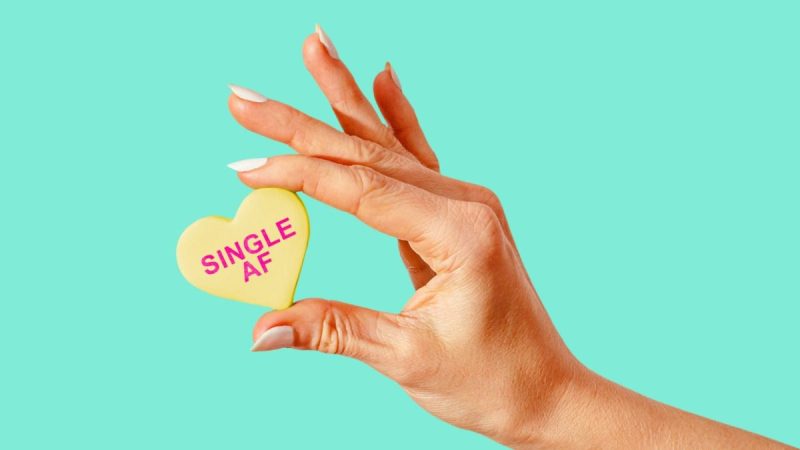 Woman's hand holding a yellow heart that says "Single AF"