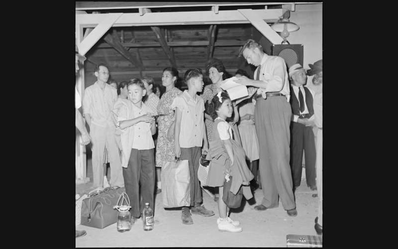 group of Japanese children and adults standing around while white man checks papers