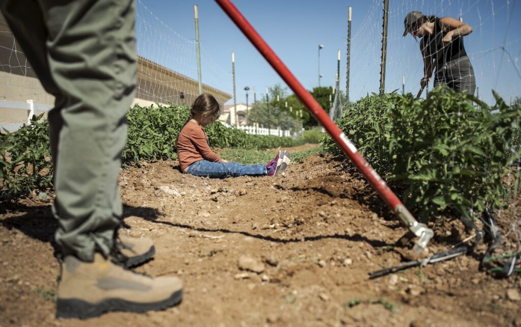 child sitting on ground as man hoes farmland
