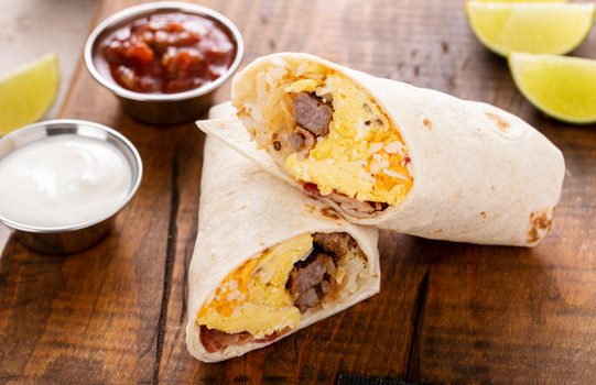 A breakfast burrito with salsa and sour cream on the side.