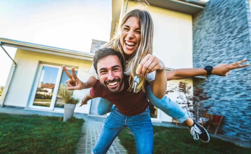 a young man and woman smile while holding keys in front of a house