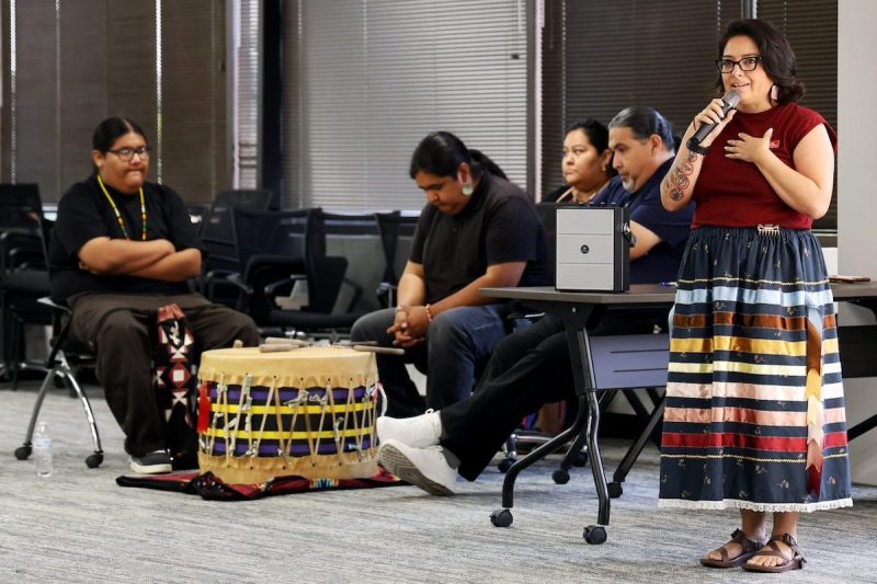 woman talking as people sit behind her with various musical instruments