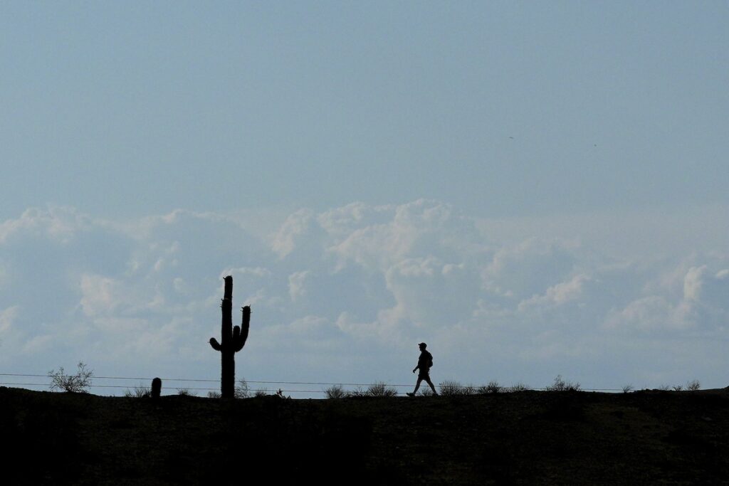storm clouds in sky as silhouette of hiker walks through