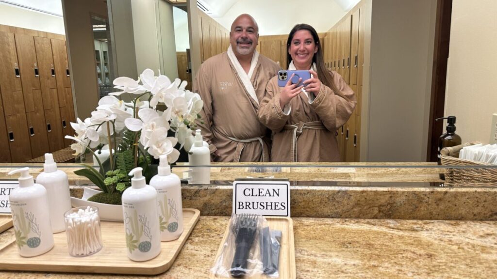 two people in robes take a smiling selfie in front of a mirror