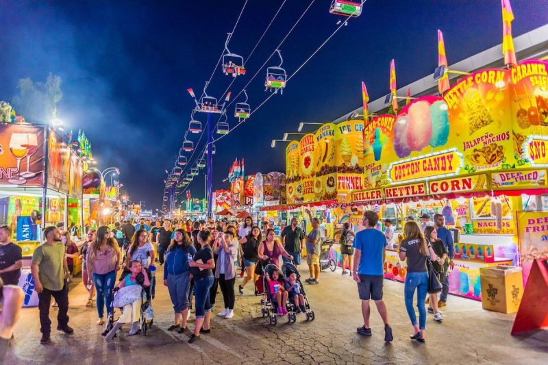 crowd of people walking through concession vendors at a state fair at night time