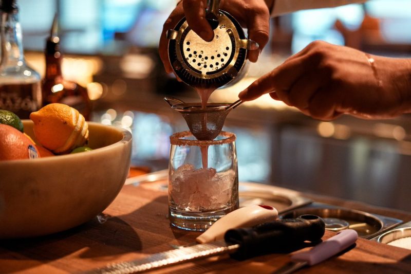 hands pouring a cocktail out of shaker at a bar