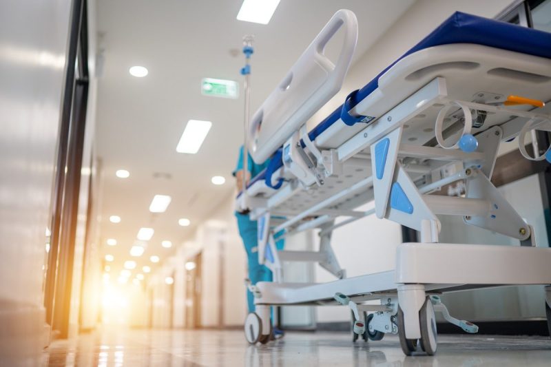 A hospital corridor with a medical staff member pushing a hospital bed.