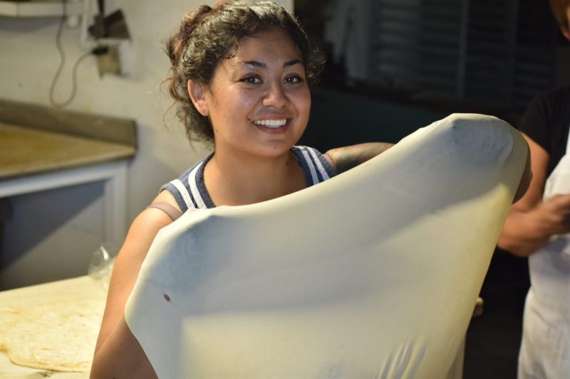 woman holding up tortilla dough inside a kitchen
